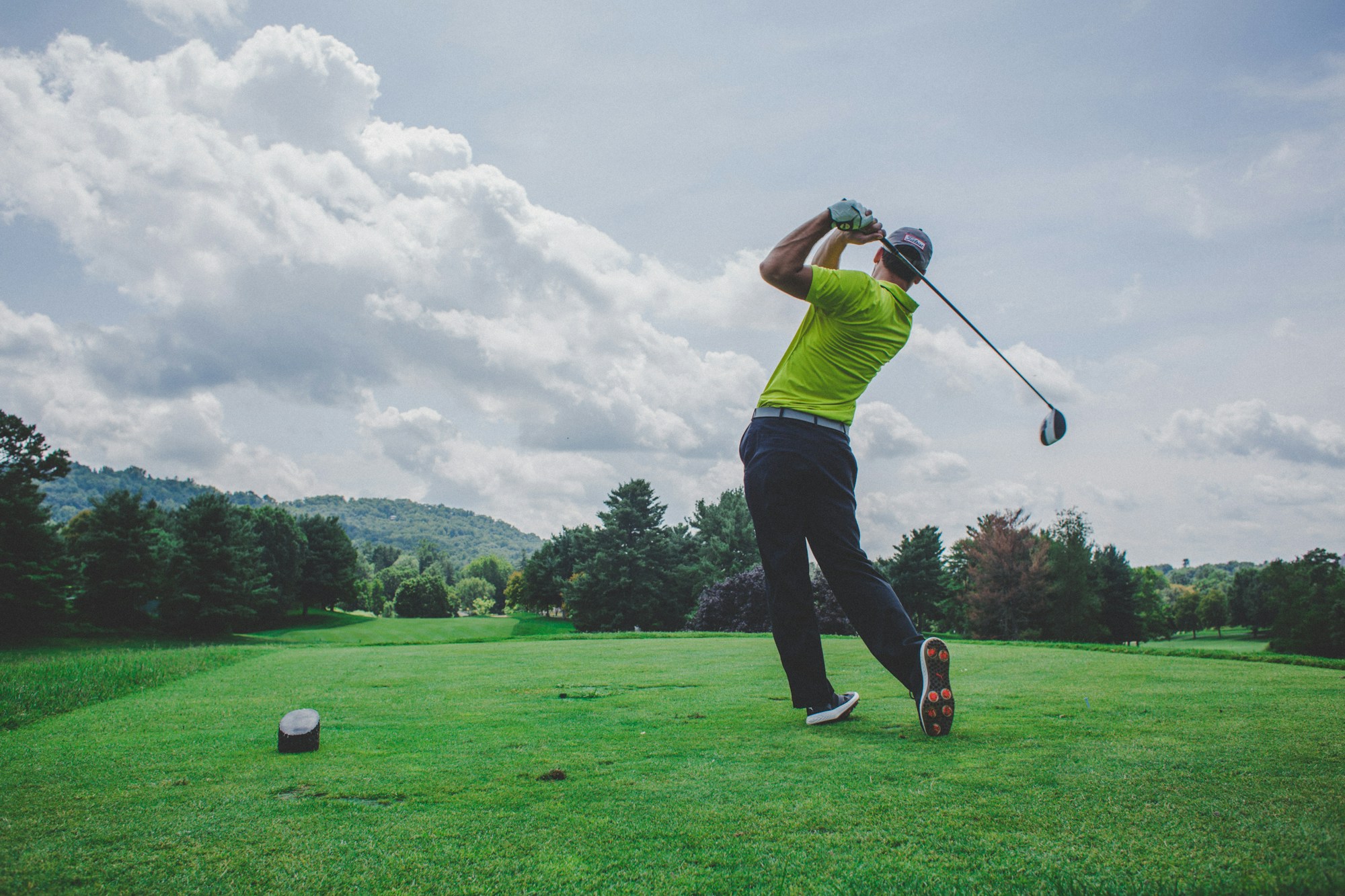 A golfer following through on a tee shot with the course stretching out behind him